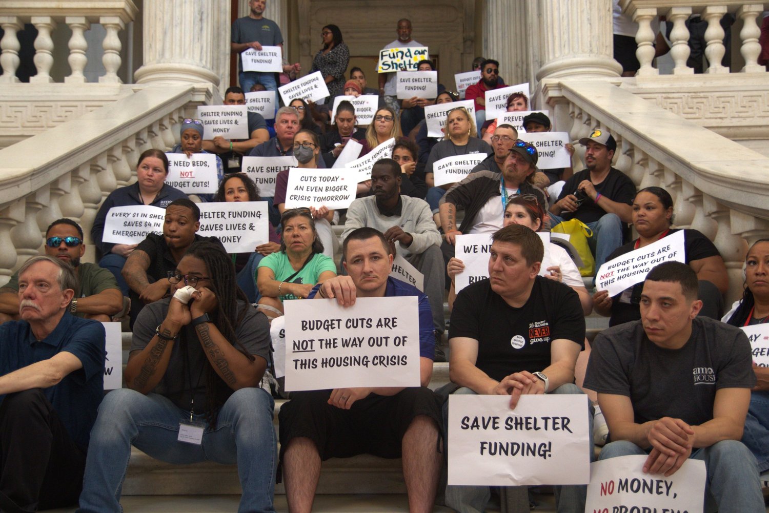 Rally on the RI State House steps with signs reading Save Shelter Funding