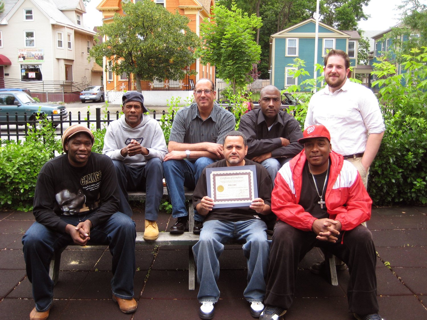 Program graduates posing outdoors, one holding a certificate