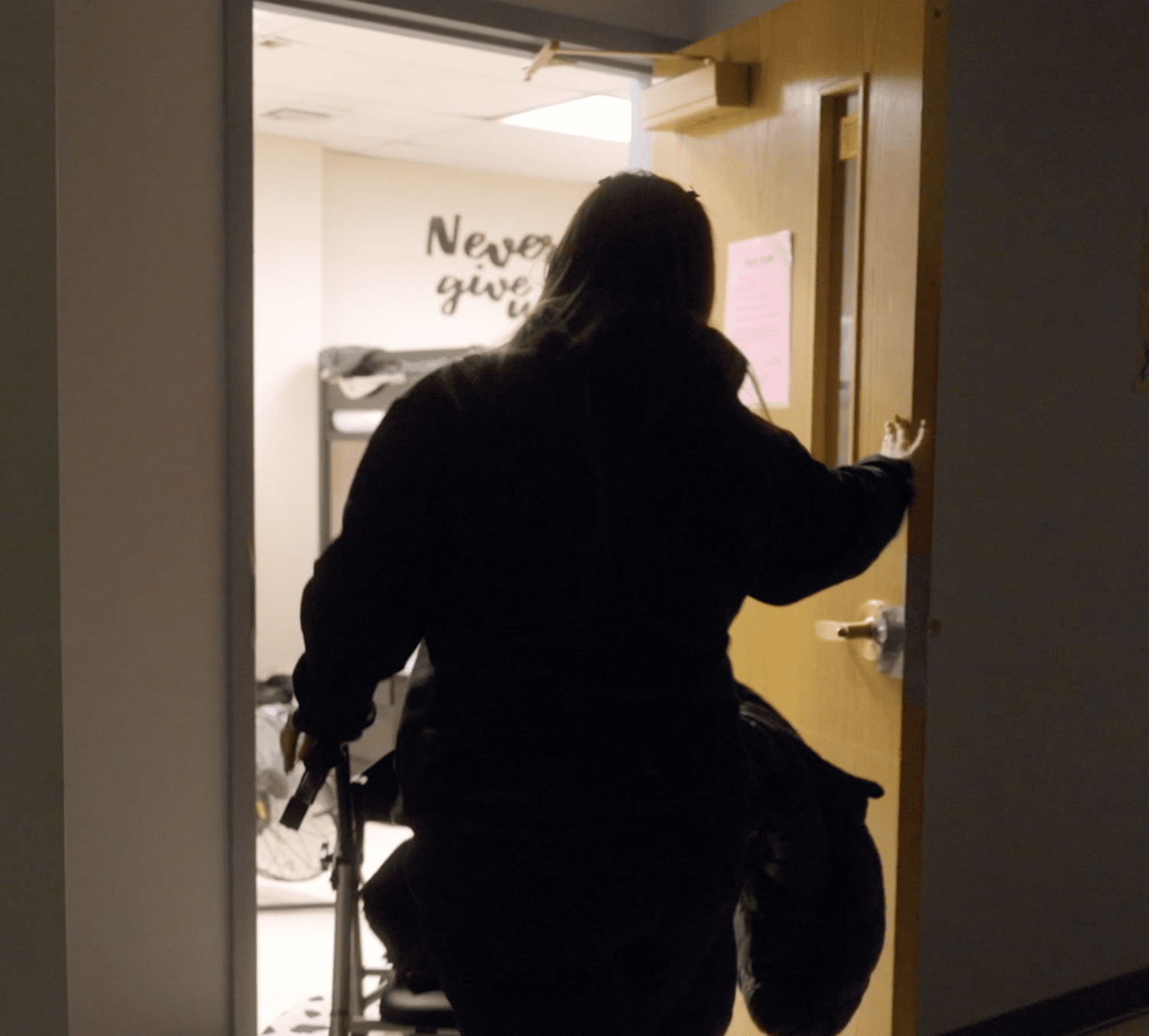 Shelter resident with a walker entering a dorm room, still from the documentary